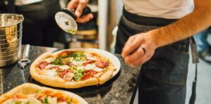 Cocinero a punto de cortar una pizza con un cortapizzas