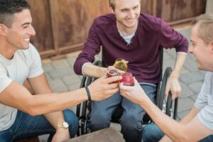 3 hombres tomando algo y festejando en la terraza de un bar. Uno de ellos está sentado sobre una silla de ruedas