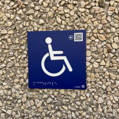 Pictograma con relieve de una silla de ruedas con código QR para poder escucharlo
