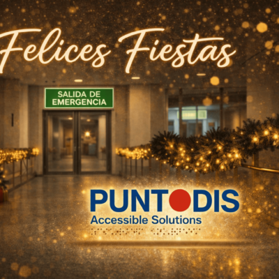 Pasillo interior decorado con luces y adornos navideños, con el mensaje “Felices Fiestas” en la parte superior, una señal fotoluminiscente de salida de emergencia visible al fondo y el logotipo de Puntodis Accessible Solutions en primer plano.