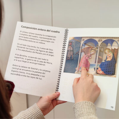 Persona explorando con el libro táctil accesible sobre La Anunciación, con ilustración en relieve y texto en braille, diseñado para facilitar la comprensión del arte a través del sentido del tacto.