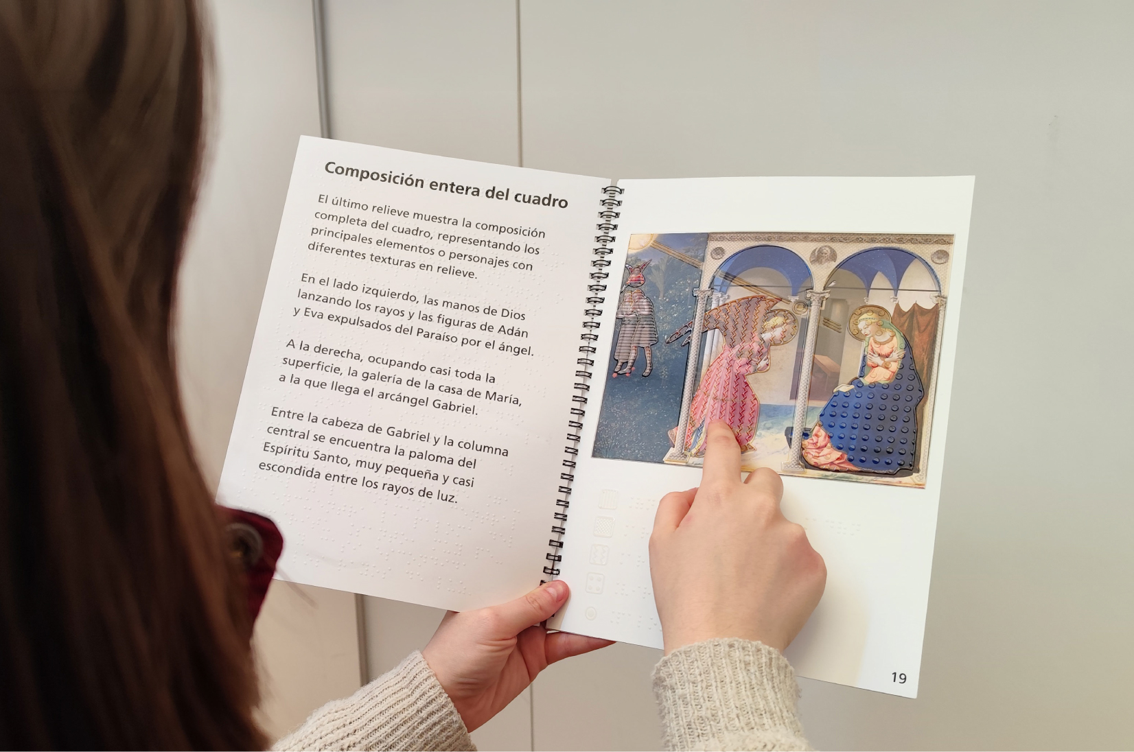 Persona explorando con el libro táctil accesible sobre La Anunciación, con ilustración en relieve y texto en braille, diseñado para facilitar la comprensión del arte a través del sentido del tacto.