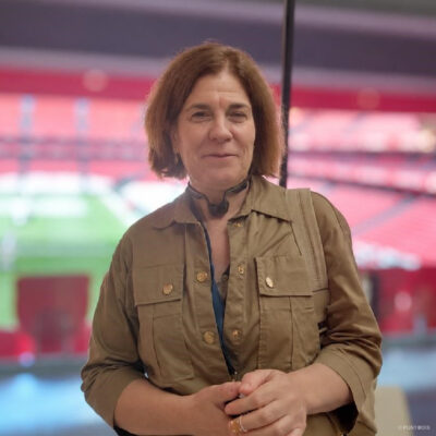 Francisca Rigo Pons, posa con una leve sonrisa y las manos juntas ante una cristalera del estadio San Mamés, al fondo el césped y las gradas rojas ligeramente desenfocados.
