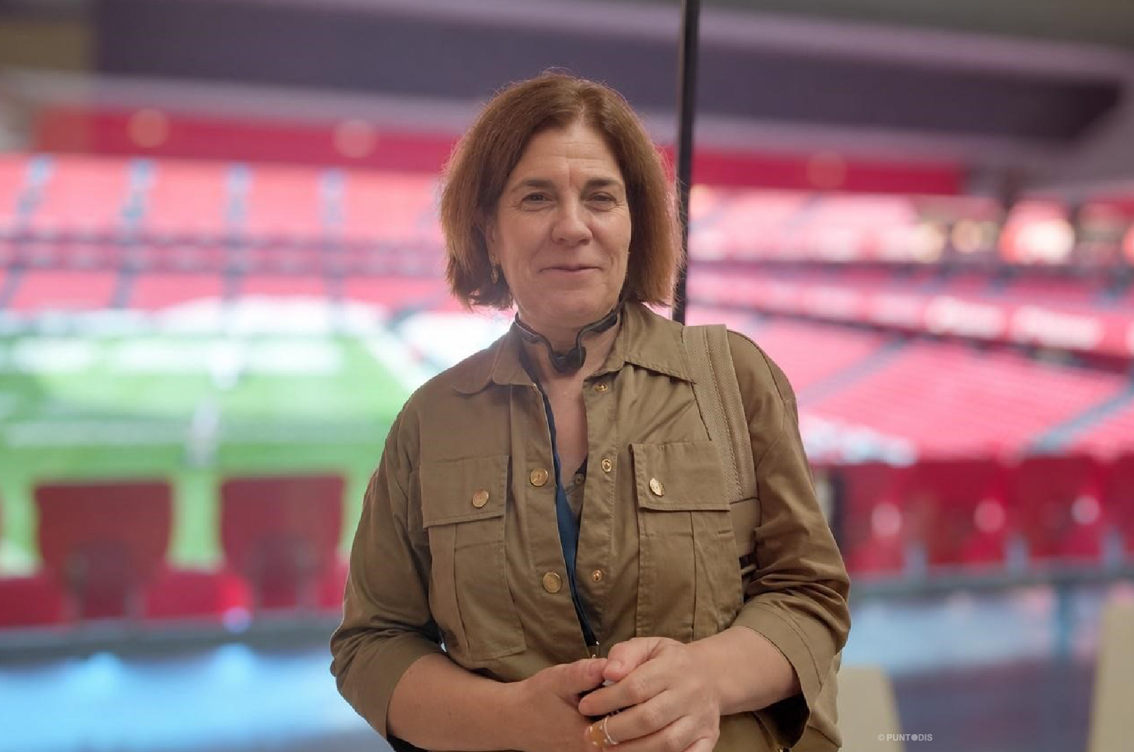 Francisca Rigo Pons, posa con una leve sonrisa y las manos juntas ante una cristalera del estadio San Mamés, al fondo el césped y las gradas rojas ligeramente desenfocados.